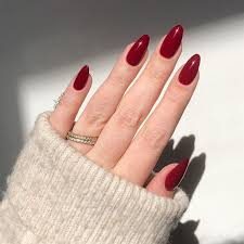 Une main affichant des ongles élégants avec une pointe française en forme de V, avec une couleur de base nude, des pointes blanches et des accents vert foncé. 