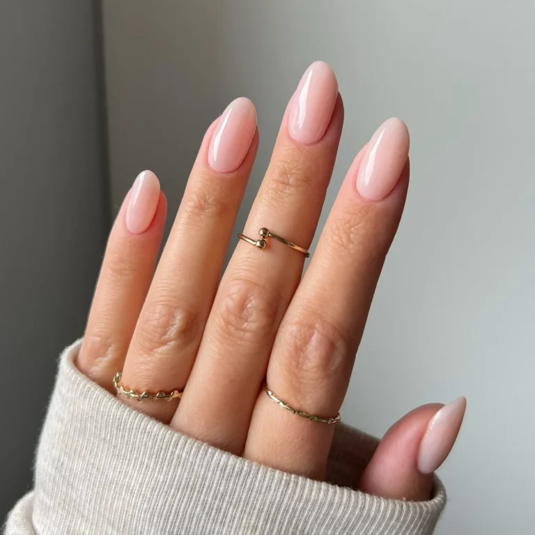 Une main aux ongles soigneusement manucurés, avec un mélange de tons brun foncé et nude, ornés de petites étoiles dorées sur deux des ongles nus. La main est partiellement recouverte d'une manche en tissu doux à motifs, et un doigt porte une bague en or au motif dentelé.
