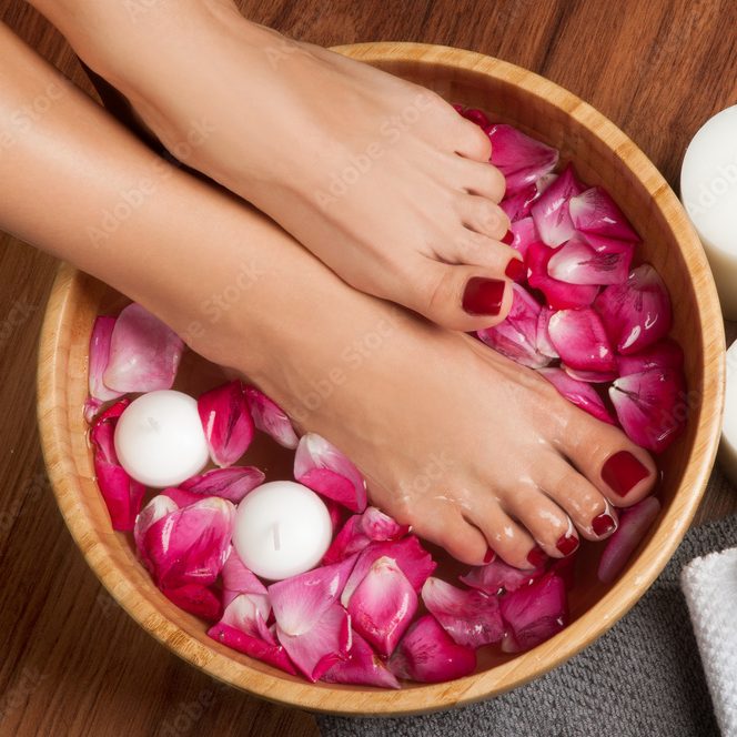 Une main aux ongles soigneusement manucurés, avec un mélange de tons brun foncé et nude, ornés de petites étoiles dorées sur deux des ongles nus. La main est partiellement recouverte d'une manche en tissu doux à motifs, et un doigt porte une bague en or au motif dentelé.